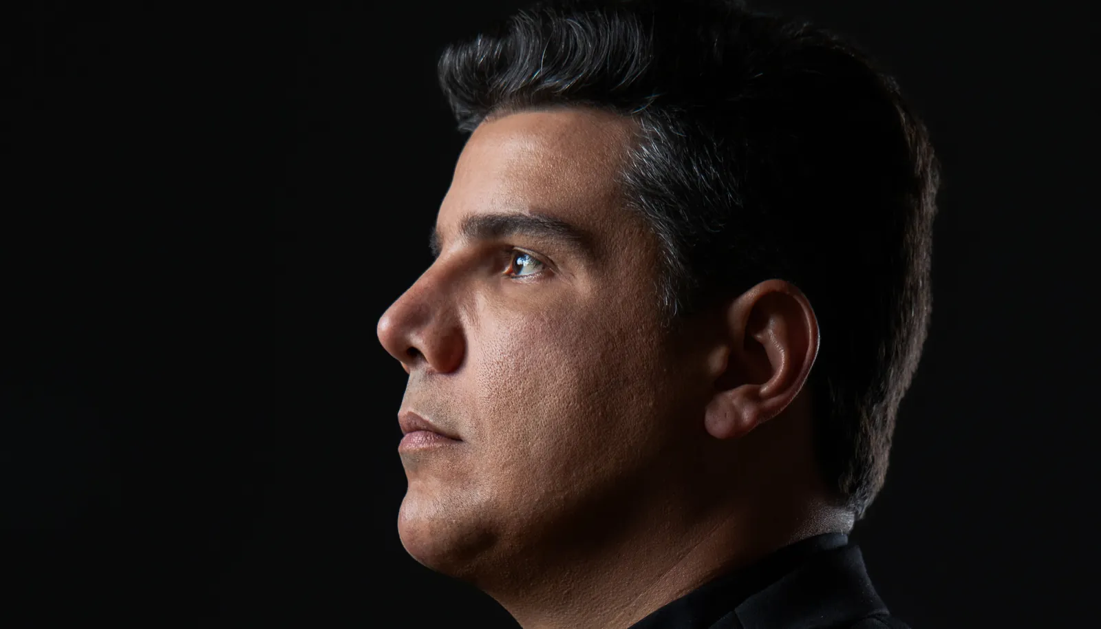 Thiago Leão Pinheiro de perfil, com iluminação lateral sobre fundo escuro