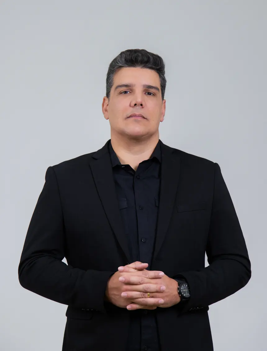 Retrato de Thiago Pinheiro de terno preto, mãos entrelaçadas