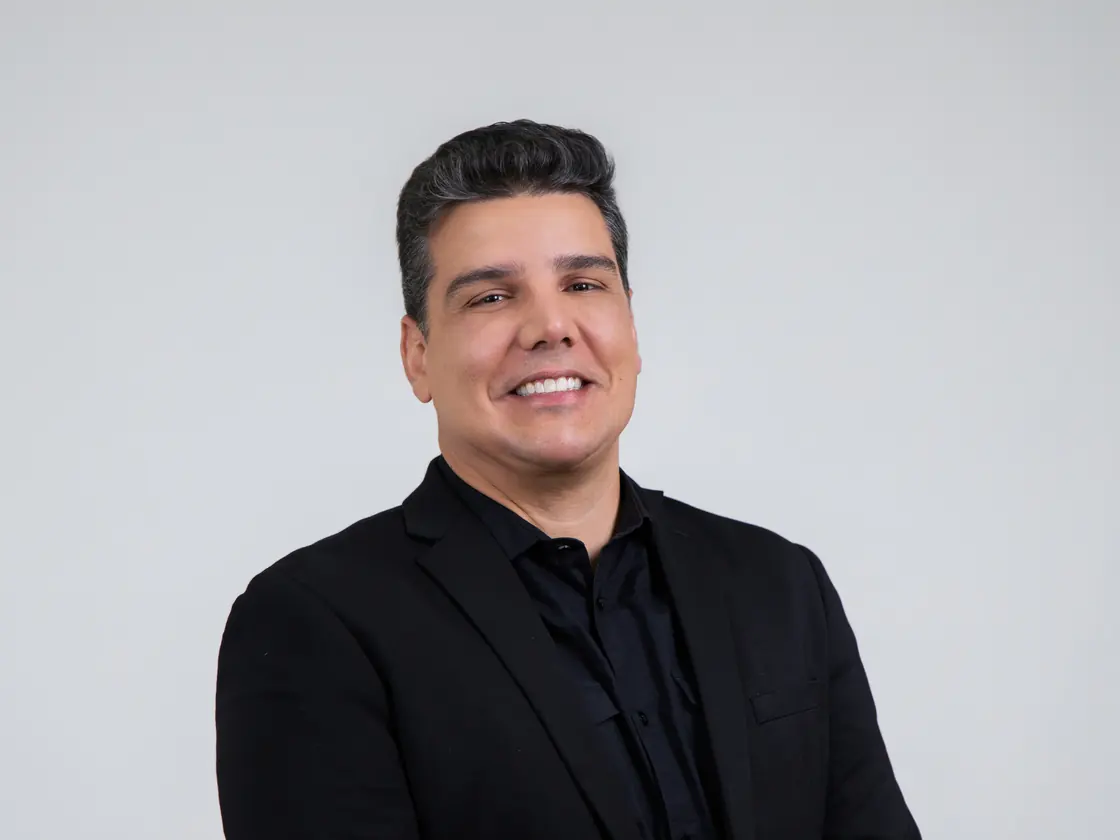 Thiago Pinheiro sorrindo, de terno preto, em fundo claro